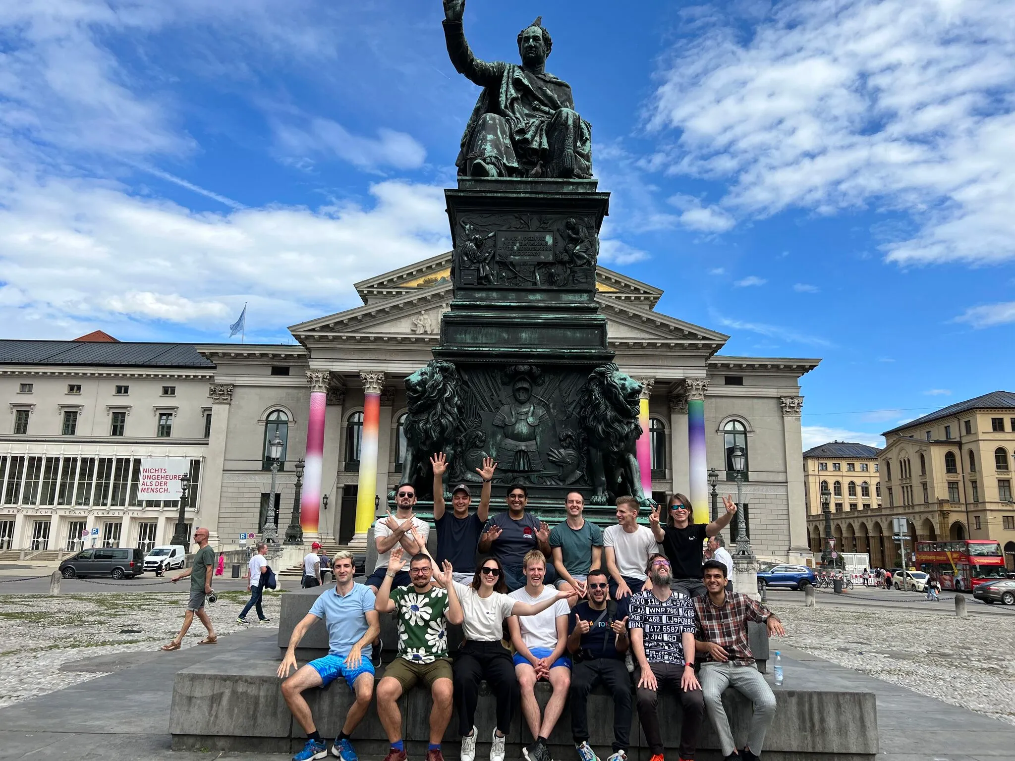Group of people posing in front of a historic statue and building under a blue sky.